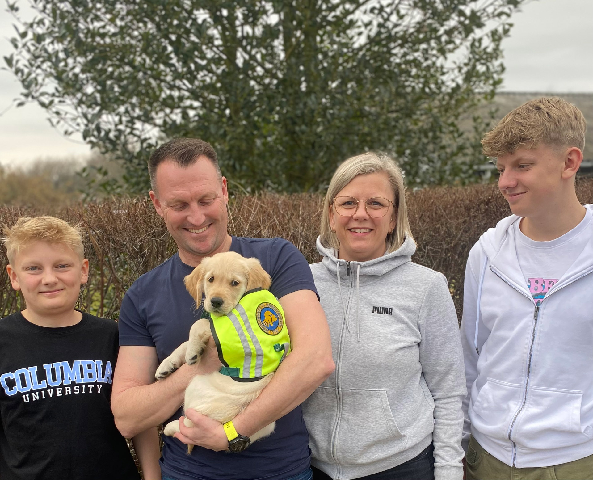 Hvalpeaspirant sammen med hvalpevært og familien udenfor