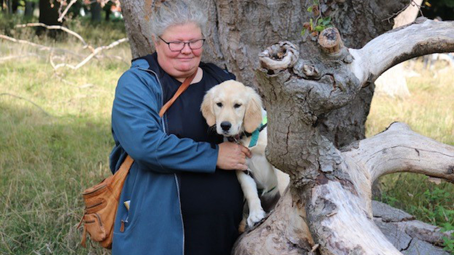 Hvalpeaspirant Inger sammen med en hvalpvært der står ved et træ