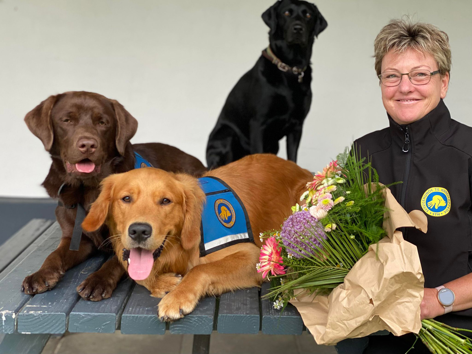 Hundeinstruktør Anette med blomster i hånden og to servicehunde ved siden af sig