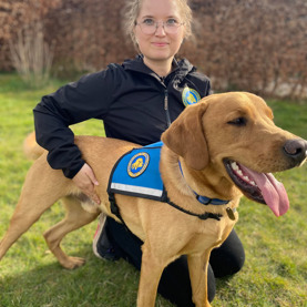 Hundetræner Sarah med en servicehund og sidder på hug