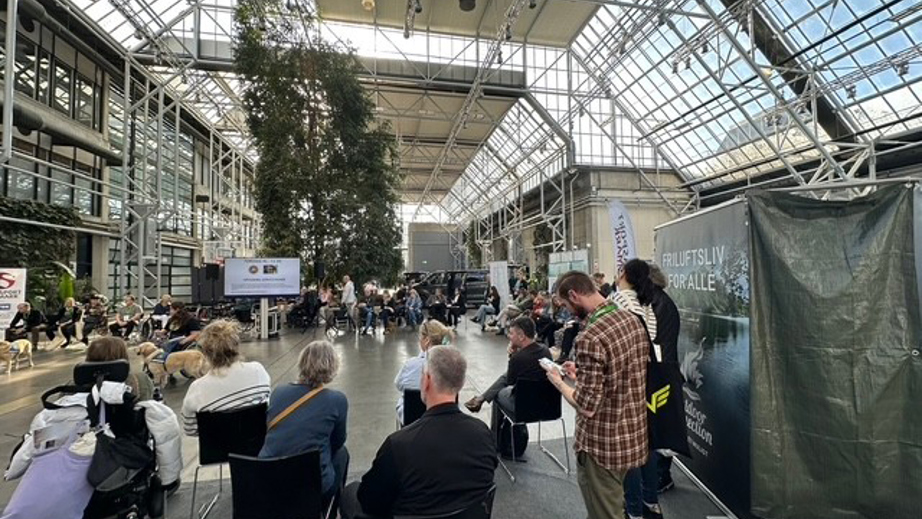 Besøgende hos STHs messestand og ser opvisning med servicehunde og brugere