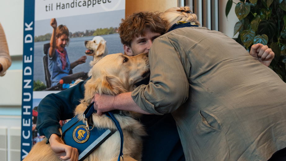 Sebastian og servicehunden Mc Kinny der får en krammer af et bestyrelsesmedlem