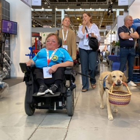 Christina og servicehund Frigga med en kurv i munden på tur i shoppingcenter