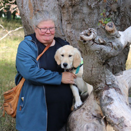 Hvalpeaspirant Inger sammen med en hvalpvært der står ved et træ