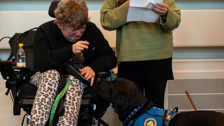 En dame holder tale mens en bruger og servicehund står ved siden af