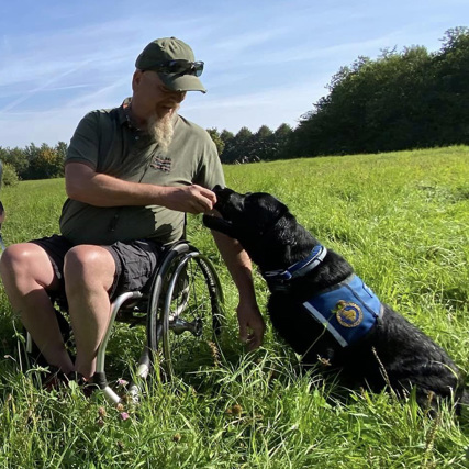 Bruger Jan og servicehund Dallas sammen udenfor i naturen og stå på en græsplæne