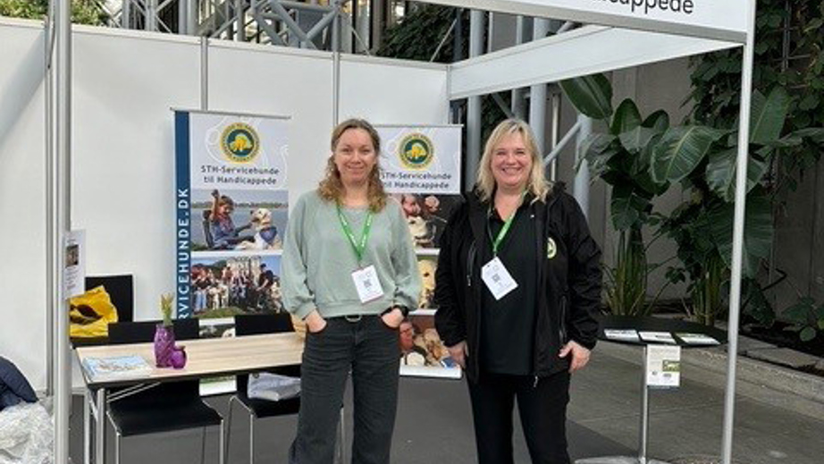 Lisa og Rikke står foran messestanden for STH servicehunde